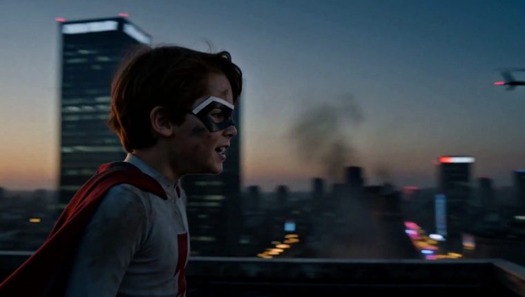 Frame from the cut: the boy on a rooftop, the city behind him at first light